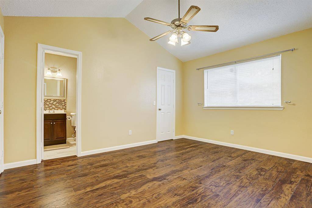 Bright bedroom with warm yellow walls, wood flooring, and a ceiling fan. Features an en-suite bathroom with modern fixtures and a large window for natural light.