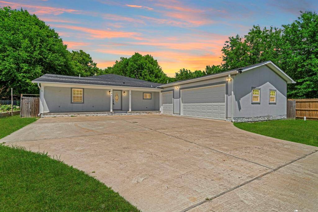 This photo shows a single-story home with a spacious driveway and a two-car garage. The exterior is well-maintained, surrounded by greenery, and features a charming porch. The sunset sky adds a warm and inviting atmosphere.