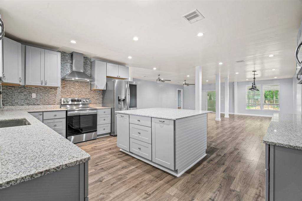 This spacious open-concept kitchen features modern stainless steel appliances, ample cabinetry, and a large central island. It seamlessly flows into a bright living area with wood flooring, recessed lighting, and large windows for natural light.