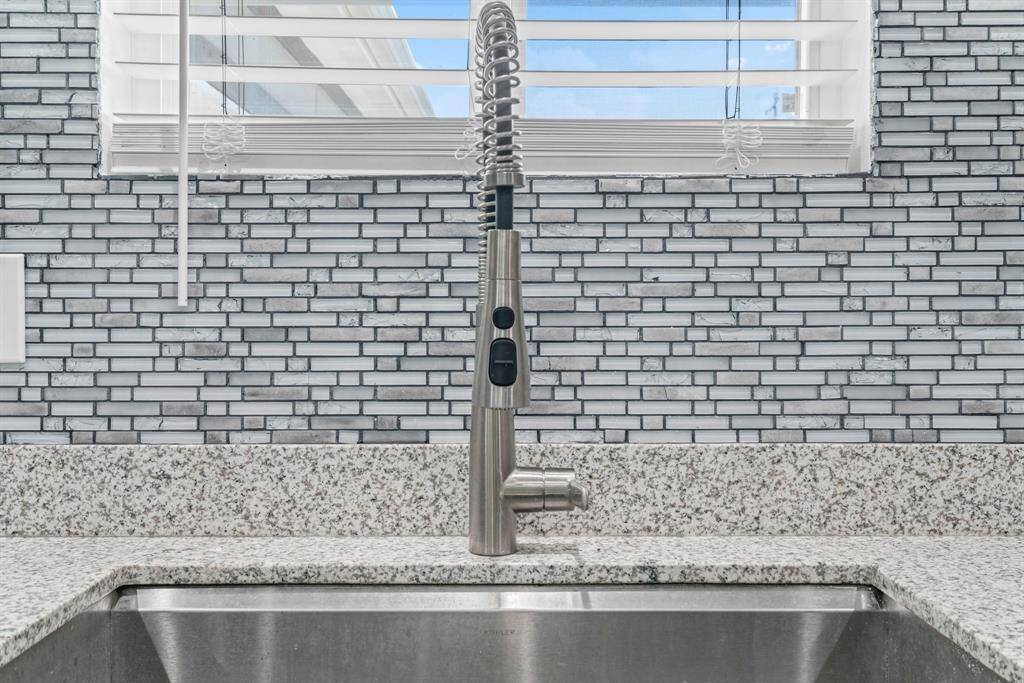 This photo showcases a modern kitchen sink with a sleek stainless steel faucet, set against a stylish mosaic tile backsplash and granite countertop, creating a clean and contemporary look.