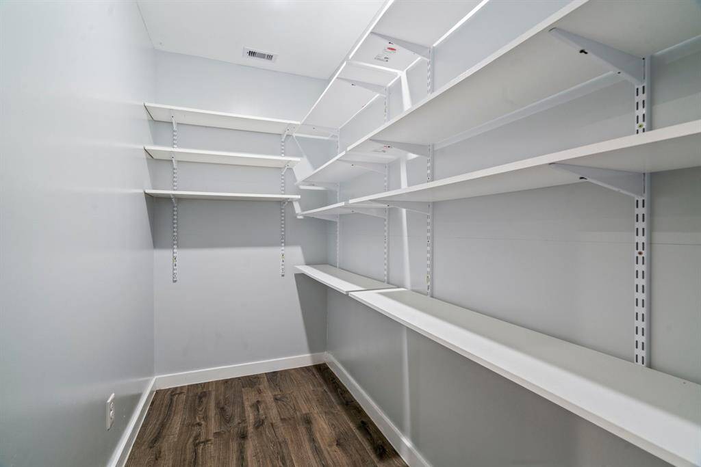 This photo shows a spacious walk-in pantry with multiple white shelves for ample storage. The room has light walls and a wood-style floor, creating a clean, organized look.