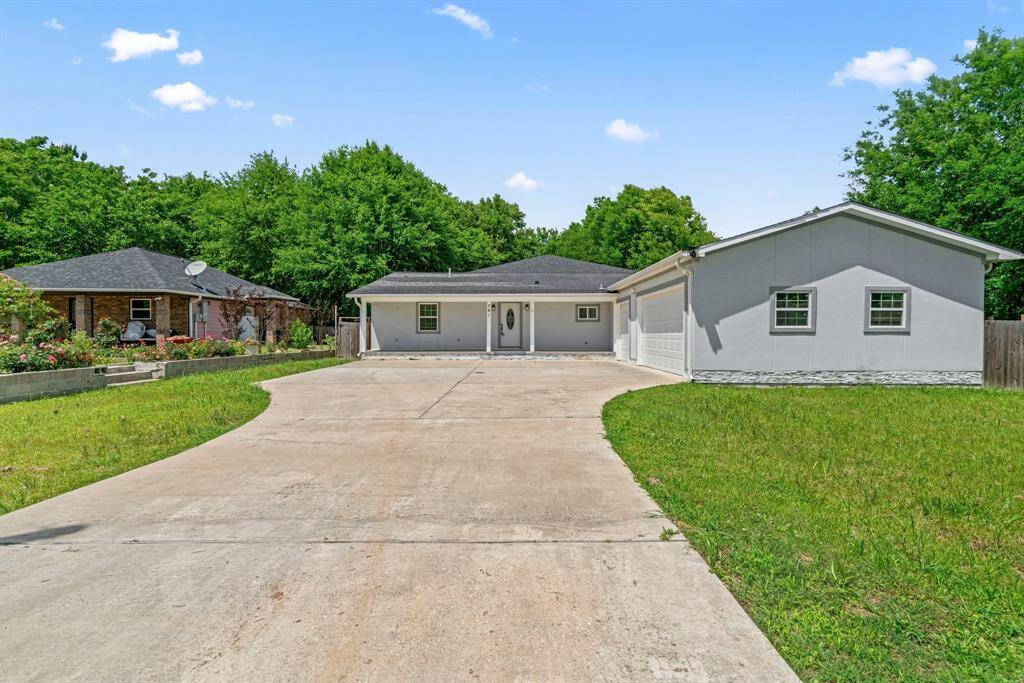 This photo showcases a single-story home with a long driveway leading to a two-car garage. The house features a simple design with a well-maintained lawn and is surrounded by lush greenery, providing a serene setting.