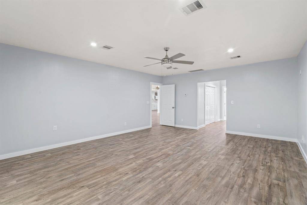 This spacious room features light gray walls, wood-style flooring, and a ceiling fan. It's well-lit with recessed lighting and provides entryways to additional rooms, offering versatile living space.