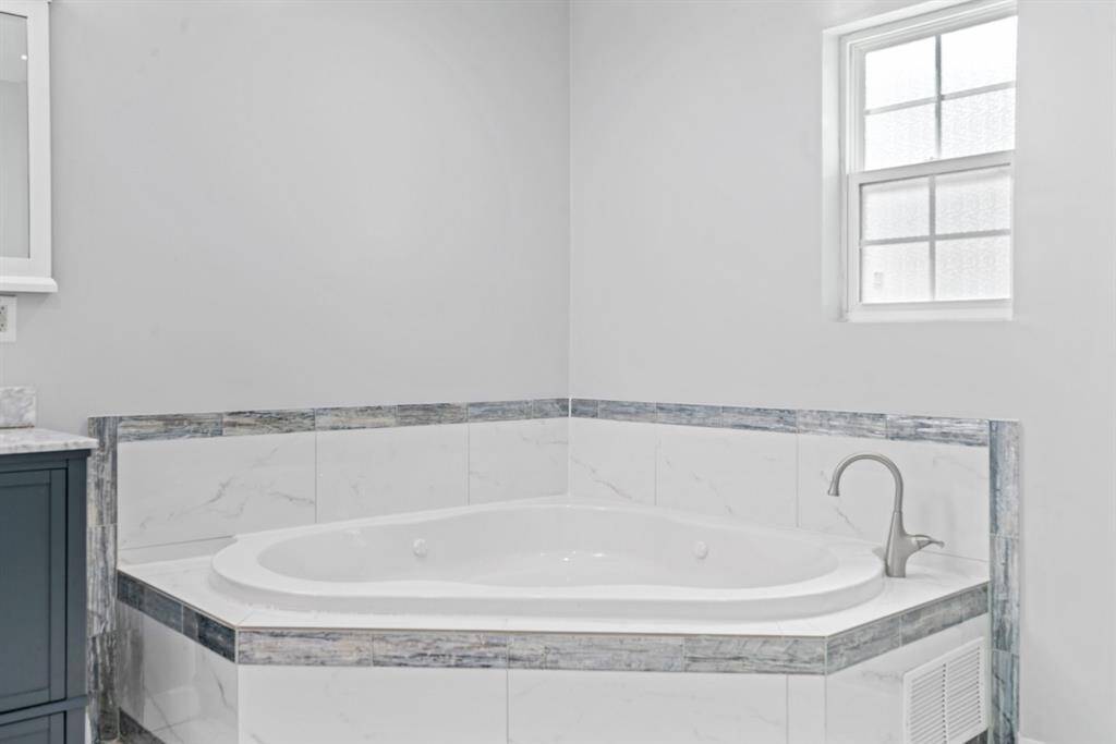 This bathroom features a corner jetted tub with elegant tile surround and a modern faucet, complemented by a window for natural light.