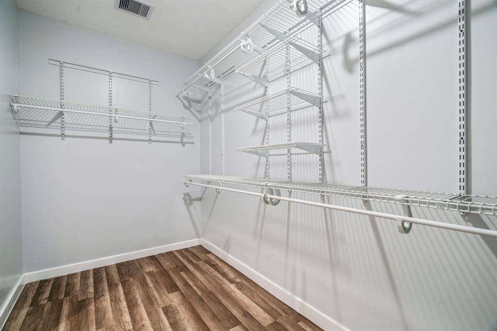 Spacious walk-in closet with ample shelving and hanging space, featuring wood-style flooring and a clean, modern design.