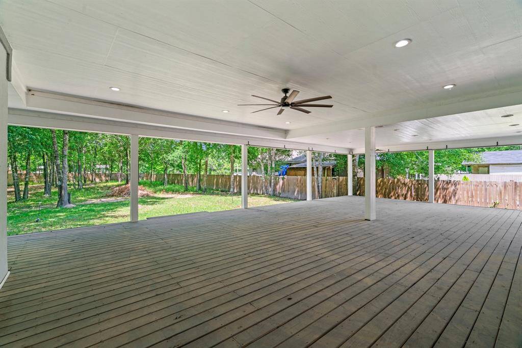 This photo showcases a spacious covered deck with a ceiling fan and recessed lighting, overlooking a fenced backyard with mature trees, ideal for outdoor entertaining and relaxation.
