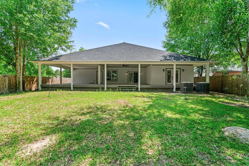 This photo showcases a spacious backyard with a covered patio area, perfect for outdoor relaxation and entertaining. The yard is fenced, providing privacy and surrounded by mature trees for shade.