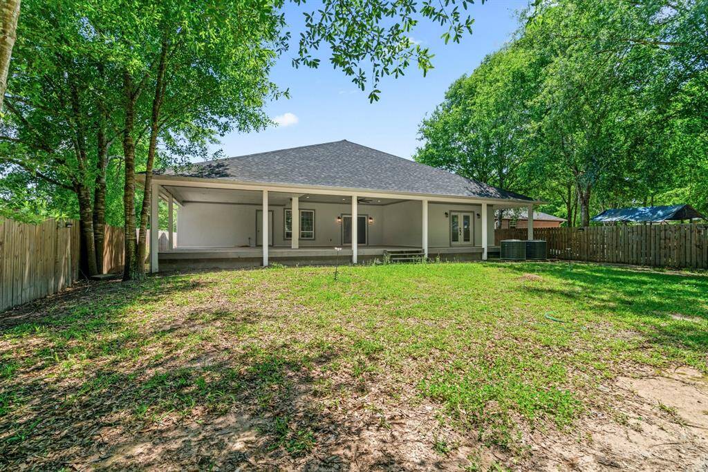 This photo showcases a spacious backyard with a covered patio, perfect for outdoor relaxation. The area is surrounded by a wooden fence, providing privacy, and features mature trees offering shade.
