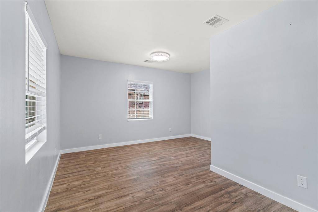 Bright, empty room with light gray walls, wood-look flooring, and two windows for natural light. Perfect for a bedroom or office space.