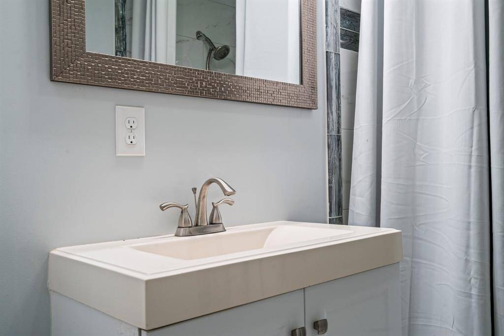 This bathroom features a modern sink with a sleek faucet, set against a light-colored wall. A textured mirror and a shower area with a curtain add style and functionality.