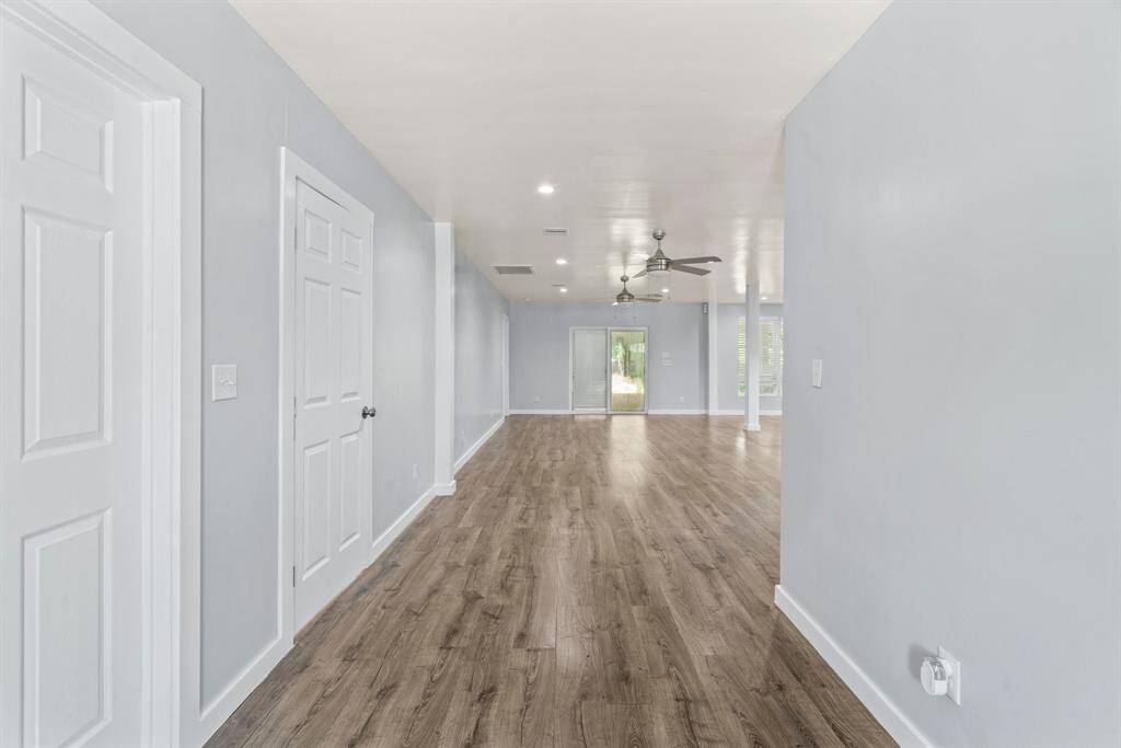 Spacious, open-concept living area with light gray walls and wood flooring. Features ceiling fans, recessed lighting, and ample natural light from glass doors leading outside.