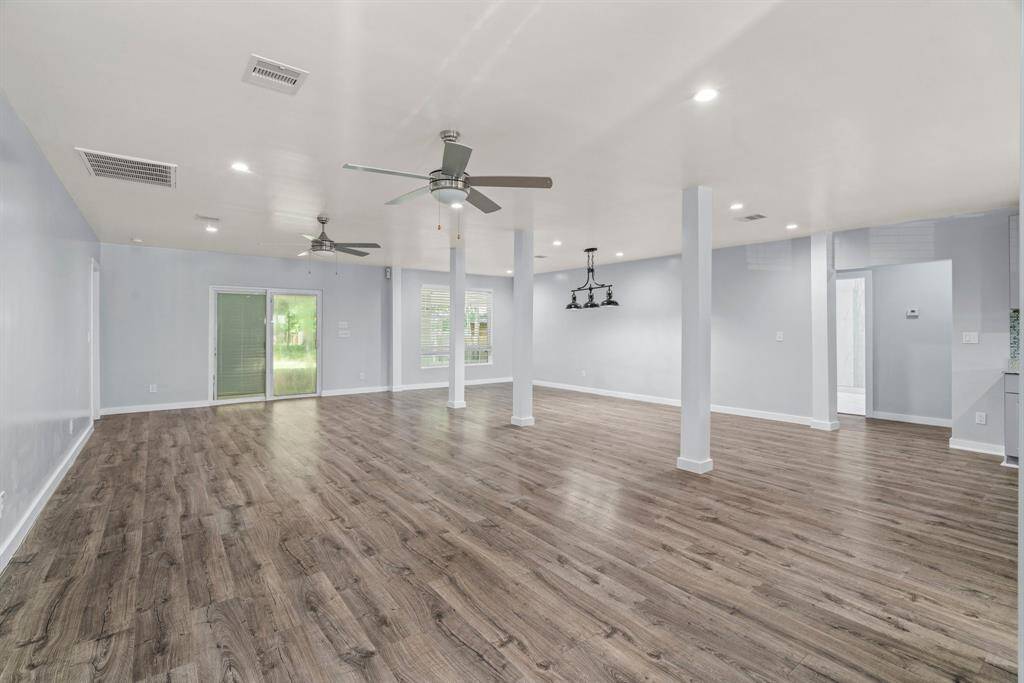 This spacious open-concept living area features stylish wood-style flooring, ceiling fans, and ample natural light from large windows and glass doors, perfect for versatile living and entertaining.