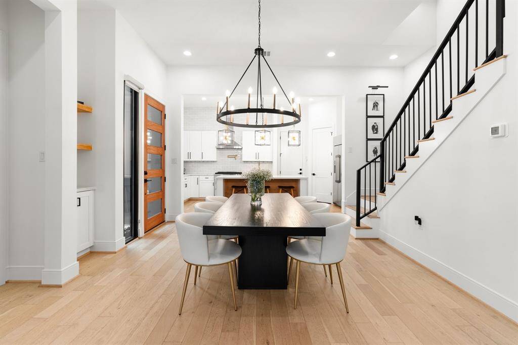 This modern dining opens to a kitchen with white cabinetry and a stylish staircase with black railing, creating a bright, contemporary space.