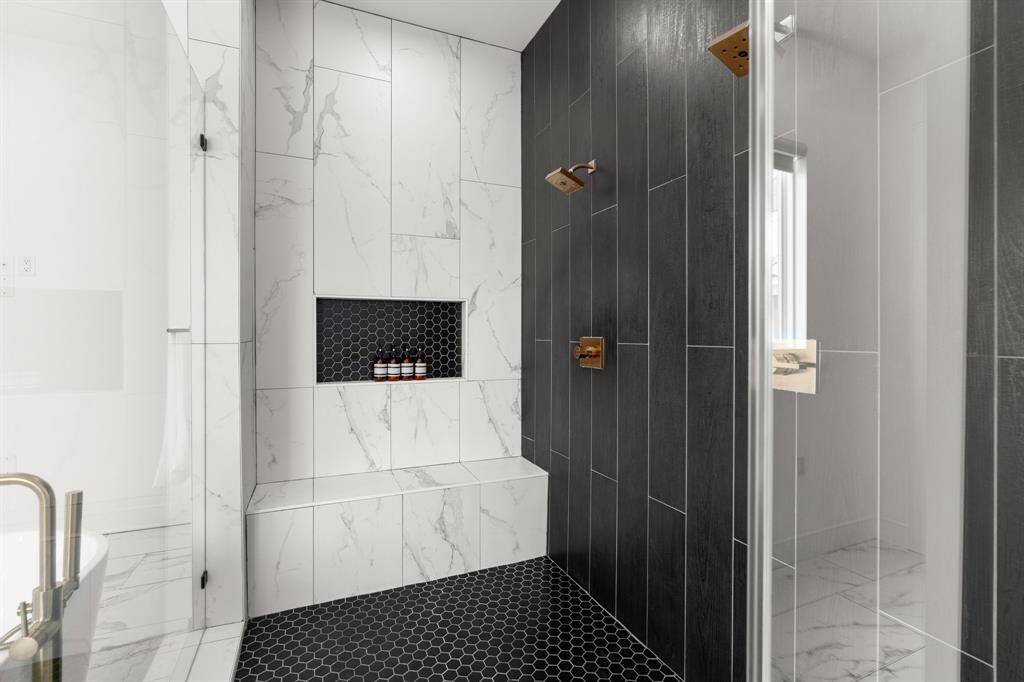 This modern bathroom features a sleek shower area with contrasting white and dark tiles, a built-in bench, and a recessed shelf. The clean lines and contemporary fixtures create a luxurious feel.