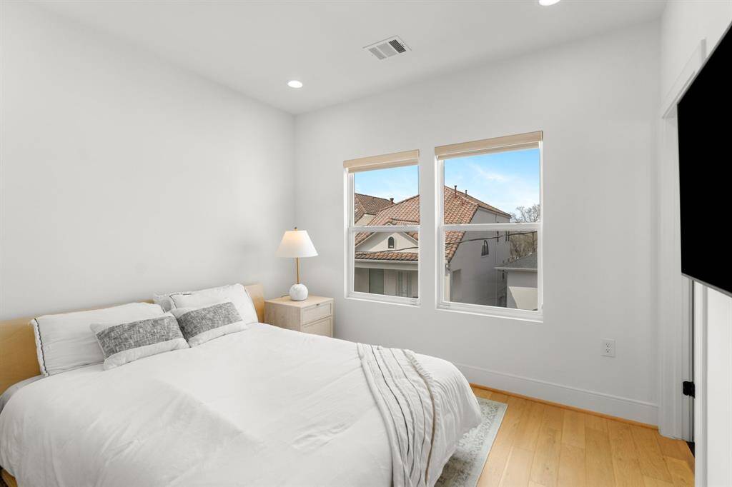 This secondary bedroom features a clean, modern aesthetic with white walls, light wood flooring, and ample natural light from two large windows, creating a bright and inviting space.