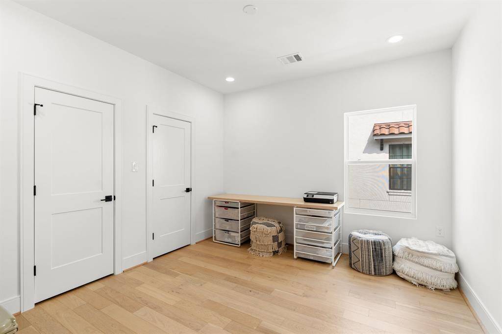 This room is a bright, minimalist space with light wood flooring and white walls and a window allowing natural light. Two doors provide access to the closet space, and direct access to a secondary bathroom.