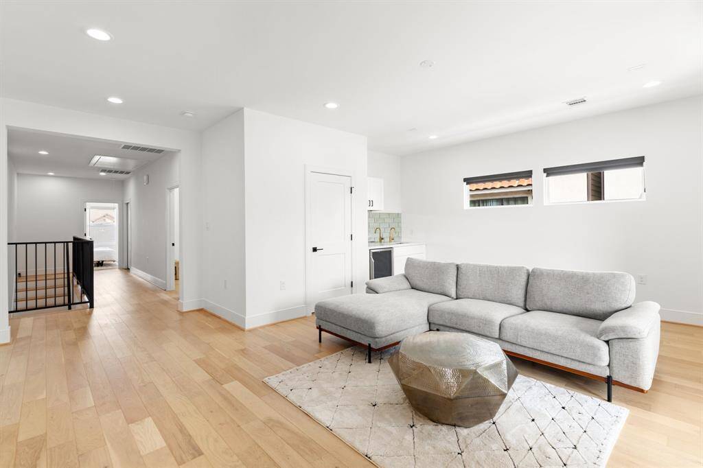 Bright and spacious enterntaiment area with modern design, featuring light wood flooring, recessed lighting and black out shades. The space includes a sleek wet bar, perfect for entertaining. Large windows provide ample natural light.