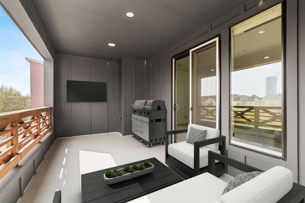 This home showcases a modern, covered balcony with sleek glass sliding doors and wooden railing, offering a view of neighboring homes. Ideal for outdoor relaxation.