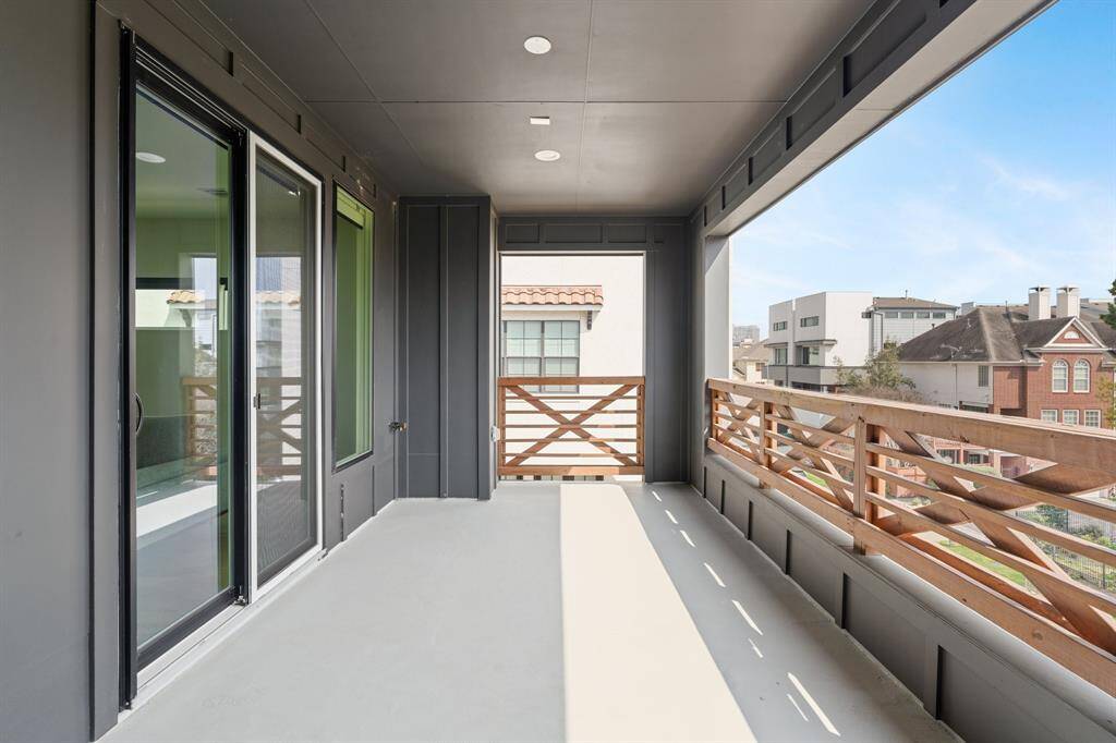 This home showcases a modern, covered balcony with sleek glass sliding doors and wooden railing, offering a view of neighboring homes. Ideal for outdoor relaxation.