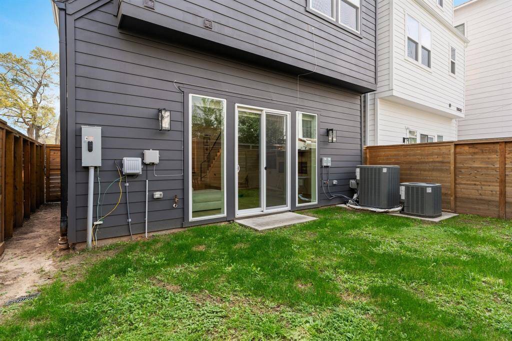 This photo showcases a modern home's backyard with a small grassy area. It features a dark exterior wall, sliding glass doors for easy indoor-outdoor access. The space is enclosed by a wooden fence, providing privacy.