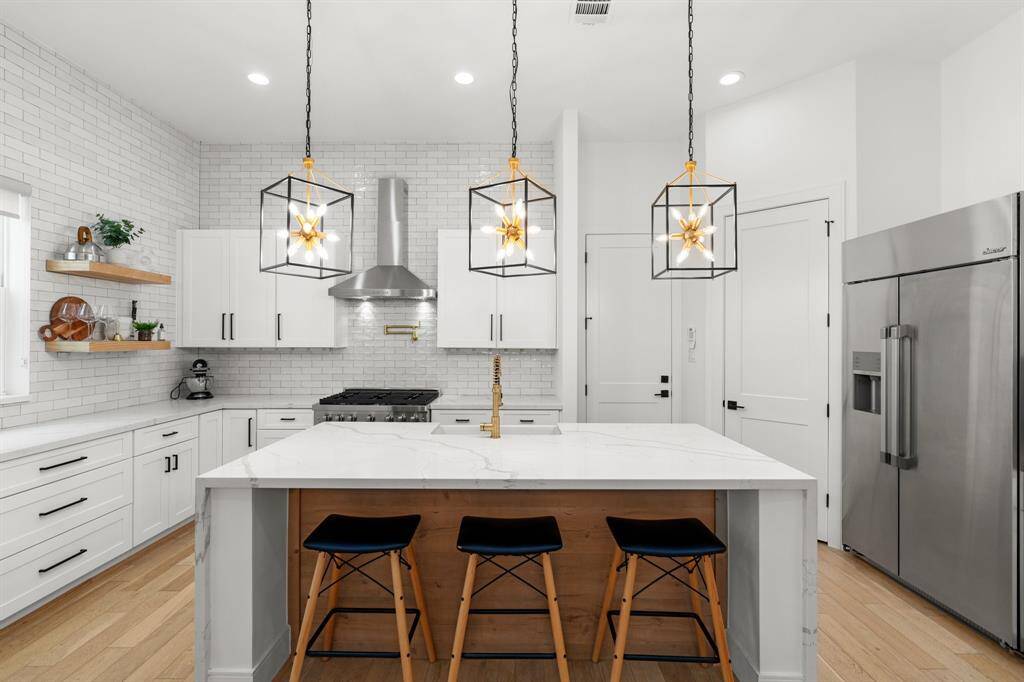 This modern kitchen features sleek white cabinetry, a large island with seating, and stylish pendant lighting. Stainless steel appliances and a subway tile backsplash complete the sophisticated look, ideal for both cooking and entertaining.