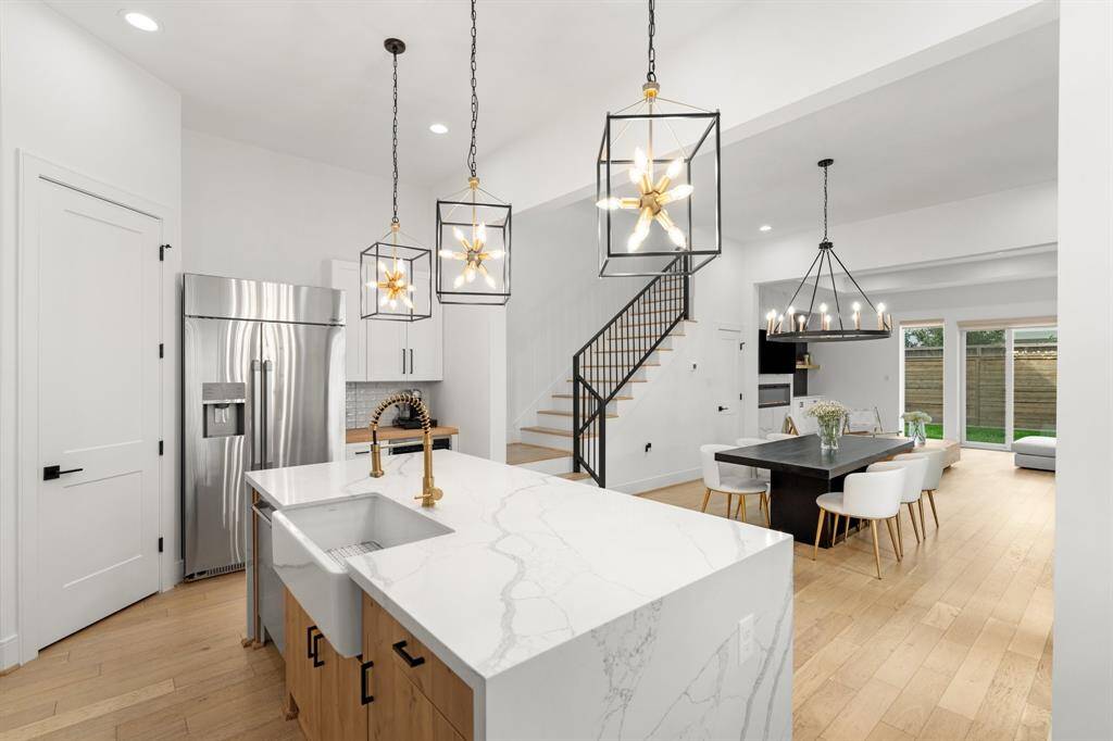 This modern, open-concept home features a bright kitchen with a large island, elegant pendant lighting, and stainless steel appliances. The dining area and living room offer seamless flow, enhanced by hardwood floors and ample natural light from large windows. Ideal for entertaining and family living.