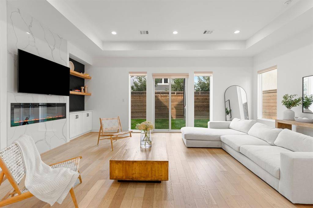 This spacious, modern living room features hardwood floors, and a sleek built-in fireplace. Natural light pours through the glass doors leading to a private backyard, creating a bright and inviting atmosphere.