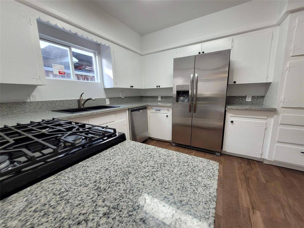 Modern kitchen with granite countertops, white cabinets, stainless steel appliances, and a gas stove. Bright and spacious with a window above the sink.
