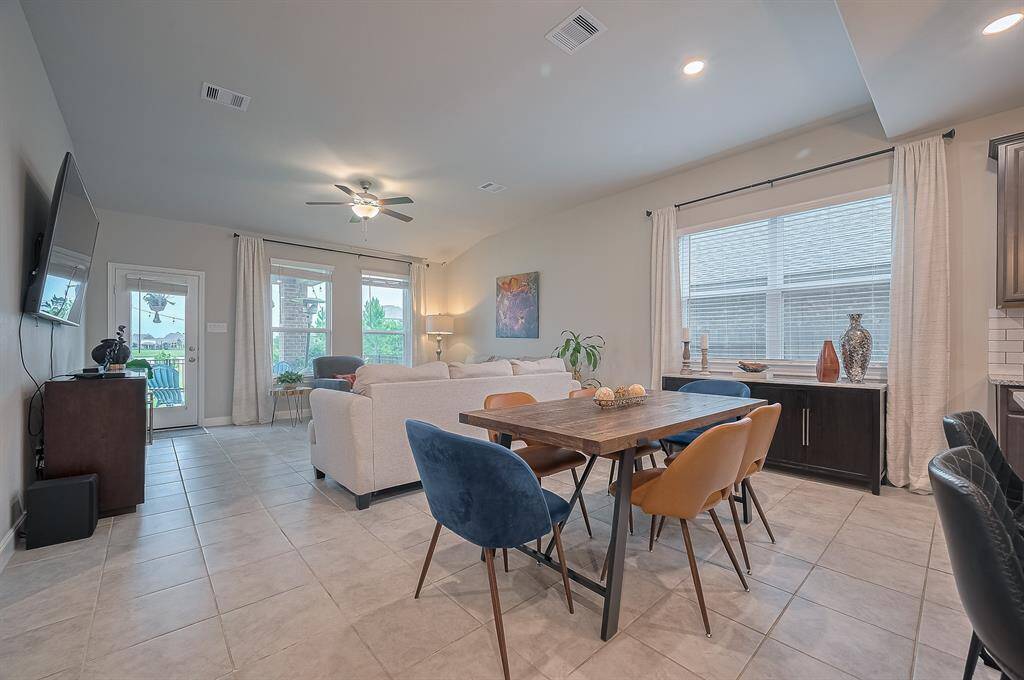 A spacious, open-concept living and dining area with a modern design. It features large windows, tiled flooring, a ceiling fan, and neutral colors.