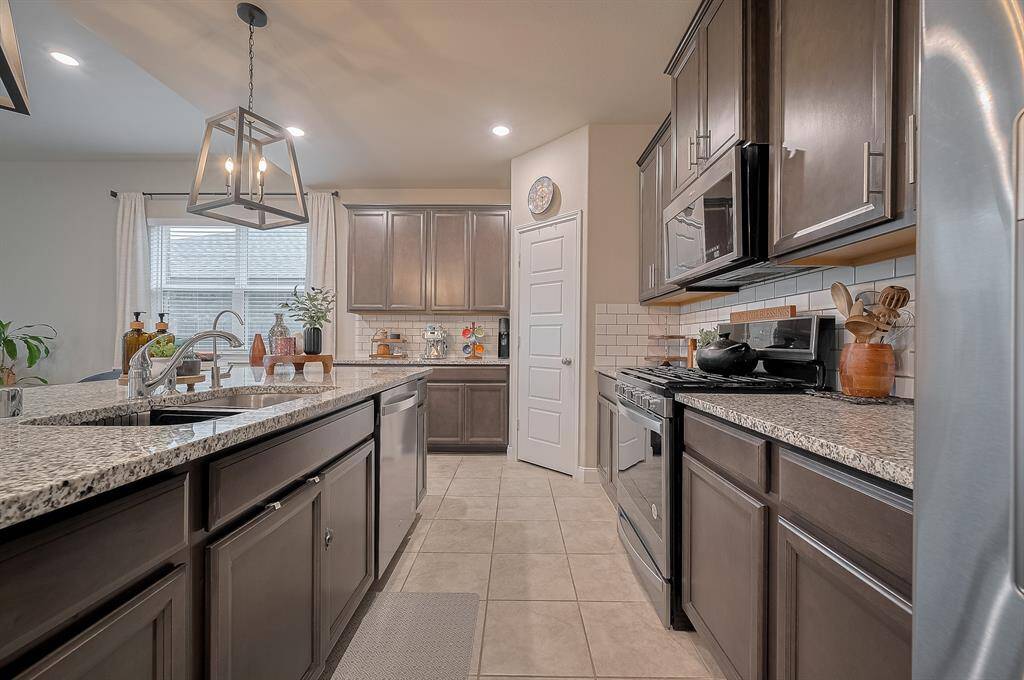 This kitchen features modern granite countertops, dark wood cabinetry, and stainless steel appliances. It has a spacious island with a double sink, pendant lighting, and a bright, open ambiance with ample natural light. Perfect for cooking and entertaining.