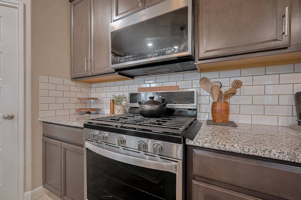 This kitchen features modern cabinetry with a sleek stainless steel stove and microwave, granite countertops, and a classic white subway tile backsplash, creating a stylish and functional cooking space.