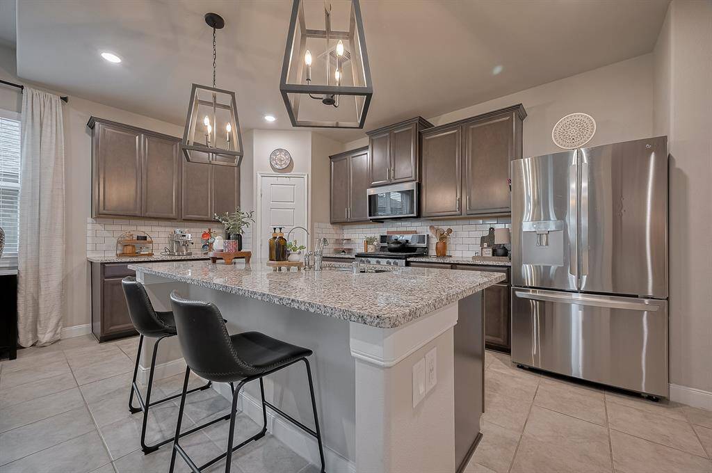 This modern kitchen features sleek granite countertops, stainless steel appliances, and dark wood cabinetry. It includes a spacious island with seating for two, pendant lighting, and a stylish subway tile backsplash, creating a warm and functional space.