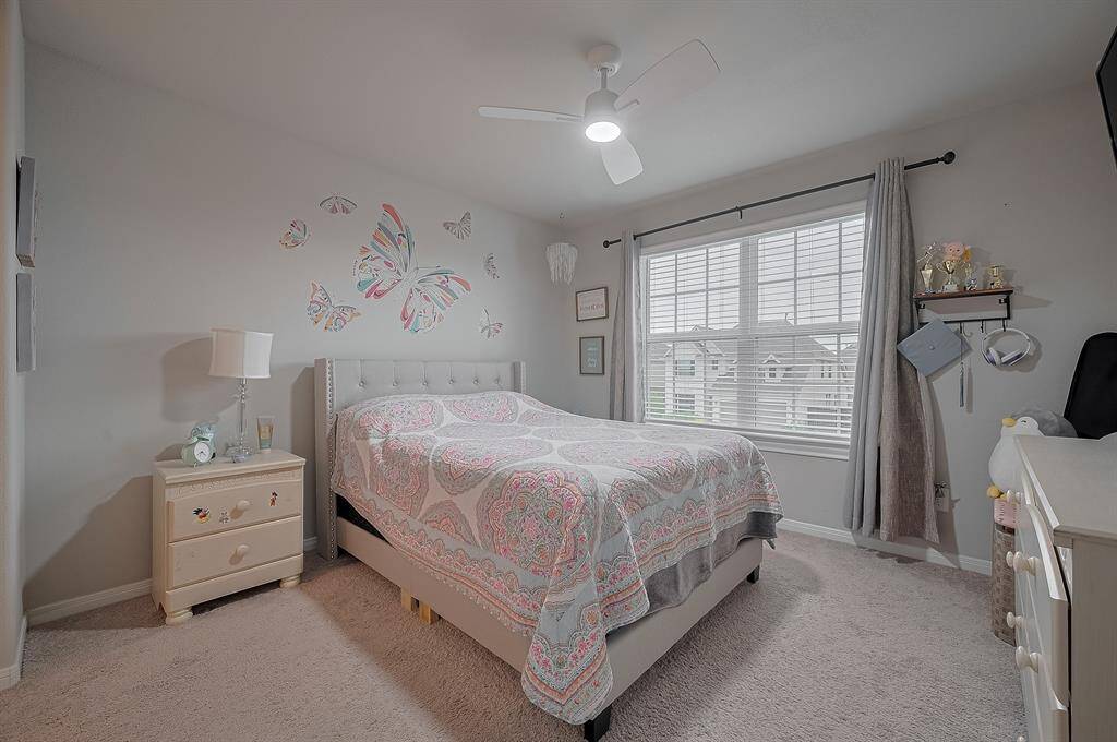 This cozy bedroom features a large window with plenty of natural light, neutral walls, and a stylish ceiling fan.