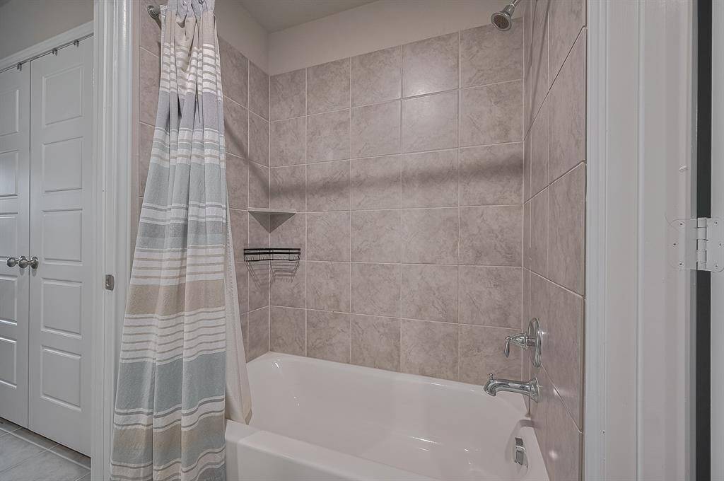 This photo shows a bathroom with a tiled shower and bathtub combo, featuring beige tiles and a striped shower curtain.
