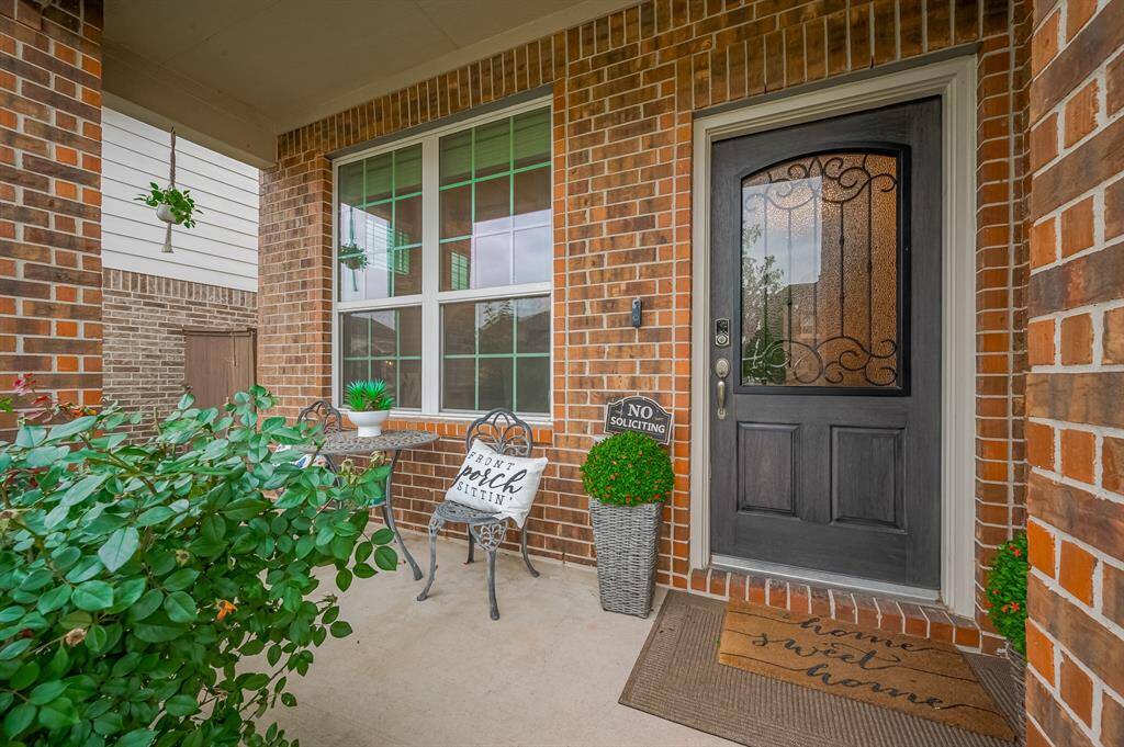 Charming front entry with a warm brick exterior, a cozy porch area perfect for relaxing, adorned with plants and inviting decor.
