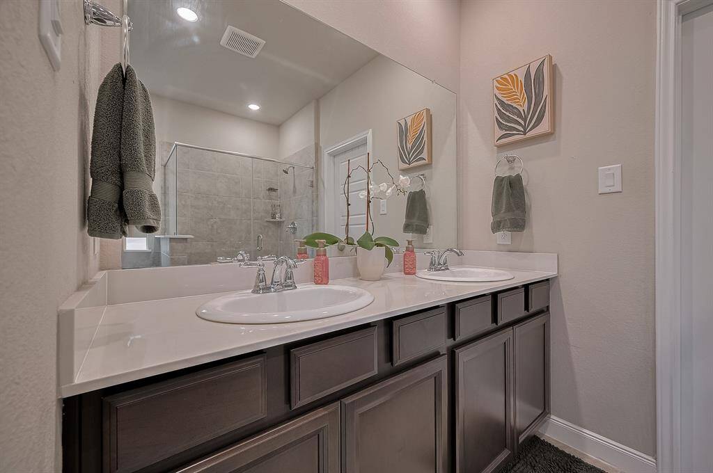 This bathroom features a modern design with dual sinks, a large mirror, and dark wood cabinetry. The space is complemented by a glass-enclosed shower and simple, elegant decor.