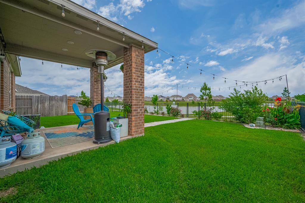 Charming backyard with a covered patio, perfect for outdoor gatherings. The lush green lawn is well-maintained, surrounded by a fence with a view of the lake.