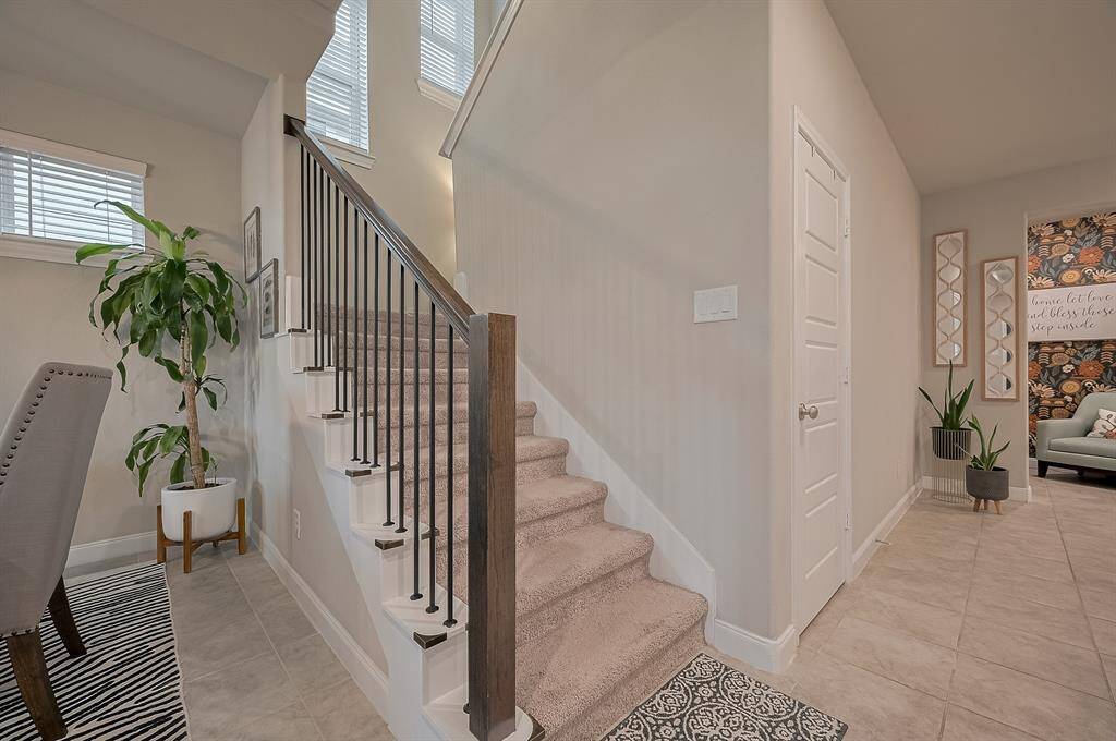 This inviting entryway features a carpeted staircase with elegant railing, neutral tile flooring, and ample natural light.