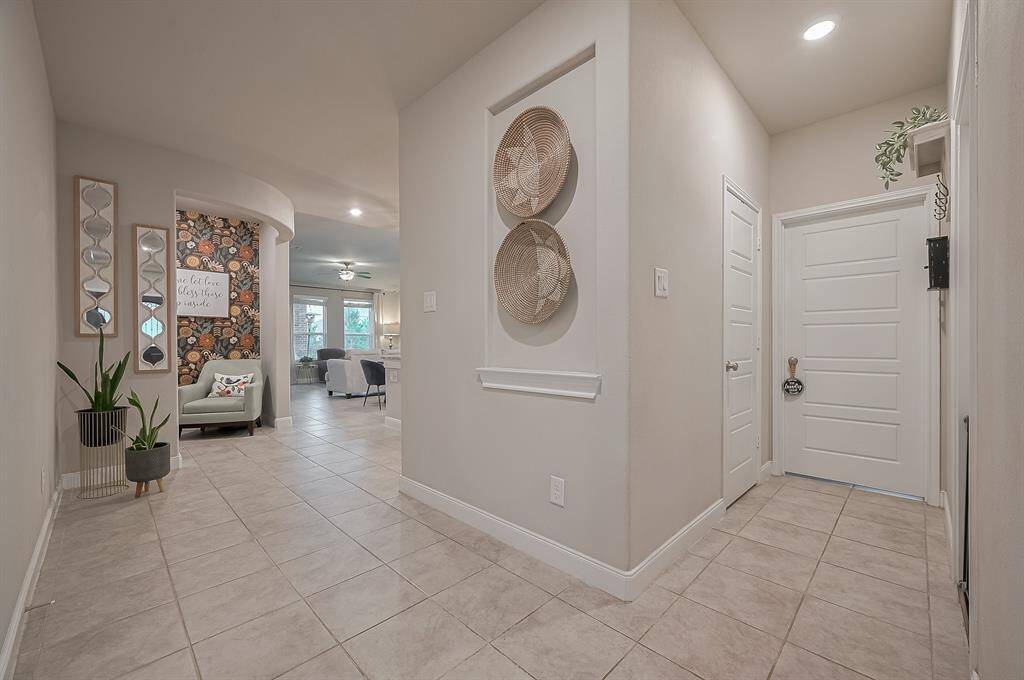 This welcoming entryway features a tiled floor leading to an open living area. A glimpse of the living room shows natural light and modern furnishings.