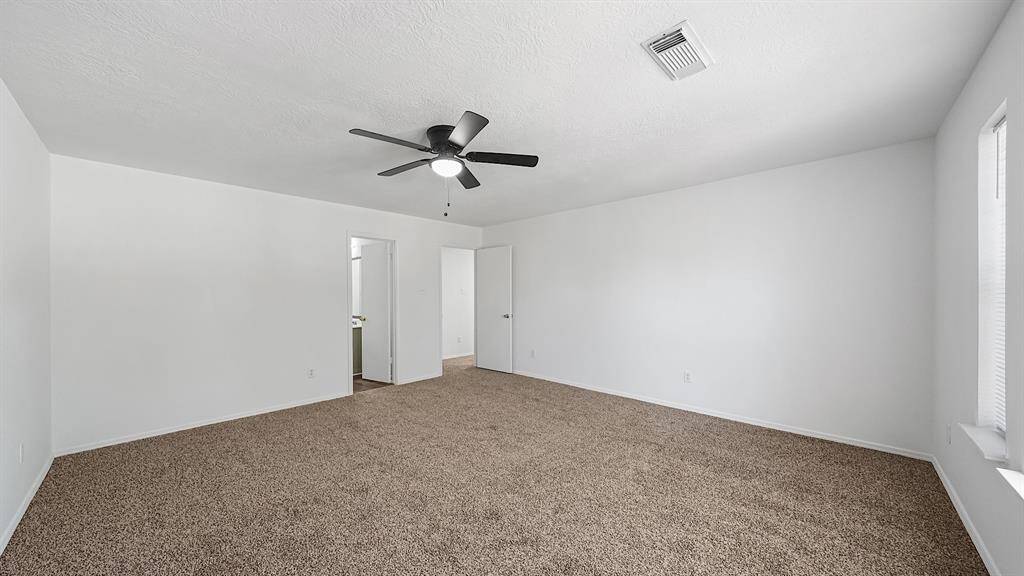 Spacious Primary bedroom shows the new carpet in the home. The modern ceiling fan is the perfect addition to this beautiful space.