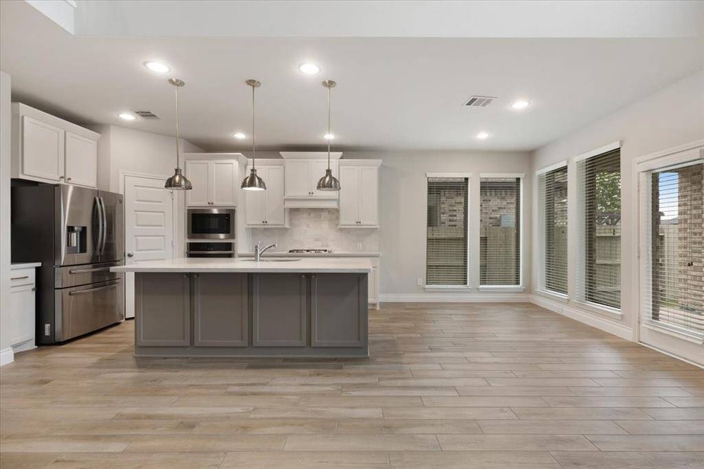 This spacious kitchen and dining area features modern appliances, a large island with pendant lighting, sleek cabinetry, and ample natural light from multiple windows, creating a bright and inviting atmosphere.