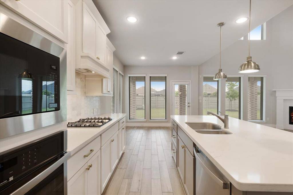 This modern kitchen features sleek stainless steel appliances, a spacious island with a sink, stylish pendant lighting, and large windows offering plenty of natural light. The open layout provides a seamless flow to the living area, perfect for entertaining.
