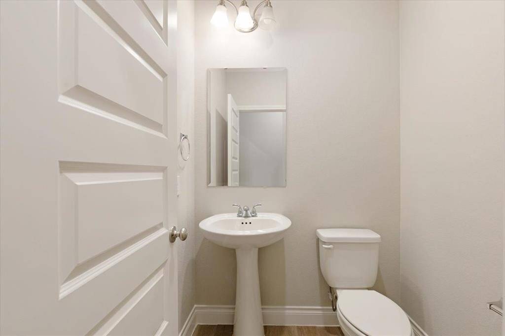 This is a compact, modern half-bathroom featuring a pedestal sink, toilet, and a wall-mounted mirror. The space is well-lit with neutral tones and a clean design.