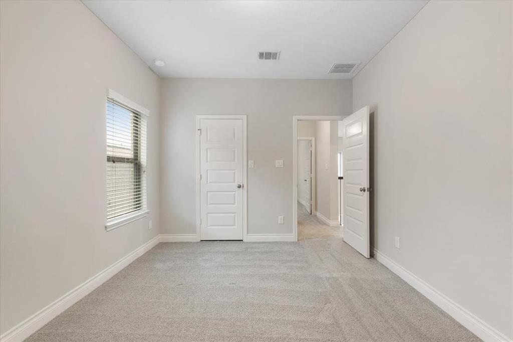This photo shows a bright, carpeted room with neutral walls, featuring a large window for natural light and two doors leading to adjacent areas. Ideal for a cozy bedroom or home office.