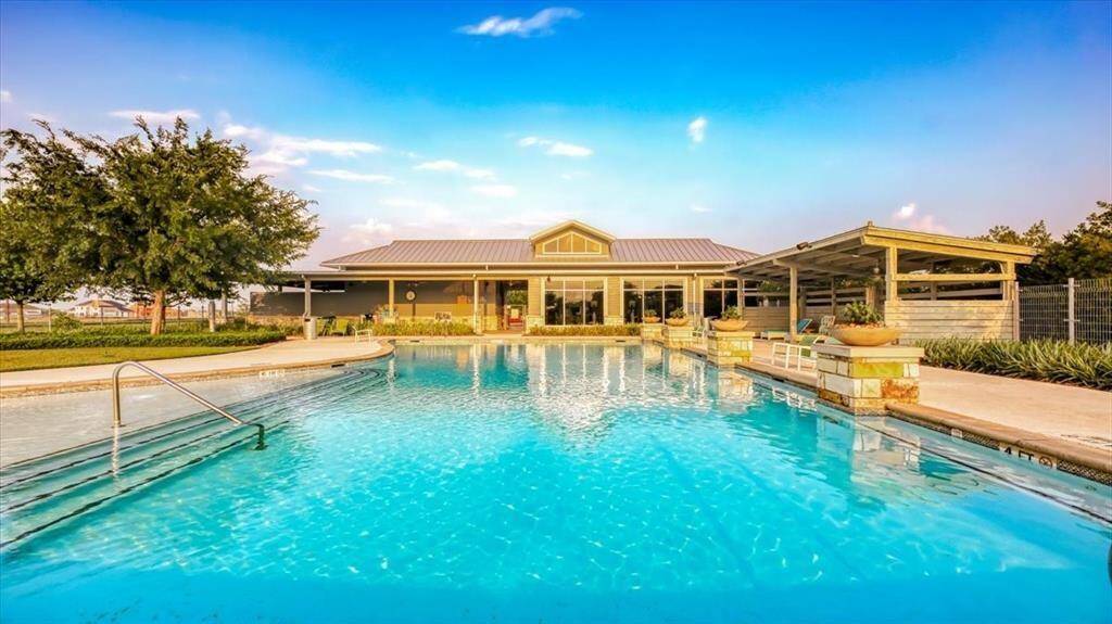 This photo showcases a beautiful outdoor pool area with a spacious patio and a modern, well-lit clubhouse in the background, perfect for relaxing and entertaining.