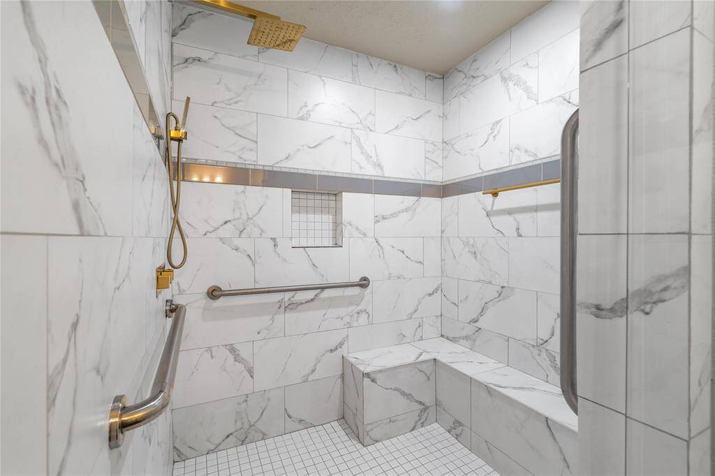 Spacious walk-in shower with marble-style tile, built-in bench seating, and a rainfall shower head with handheld wand.