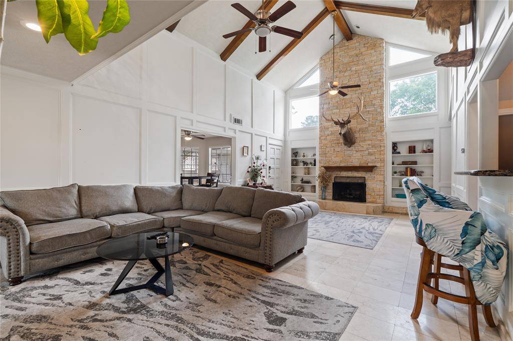 Exposed beams, a stone fireplace, and large windows create a warm yet grand atmosphere—anchoring the living space with natural light and character.