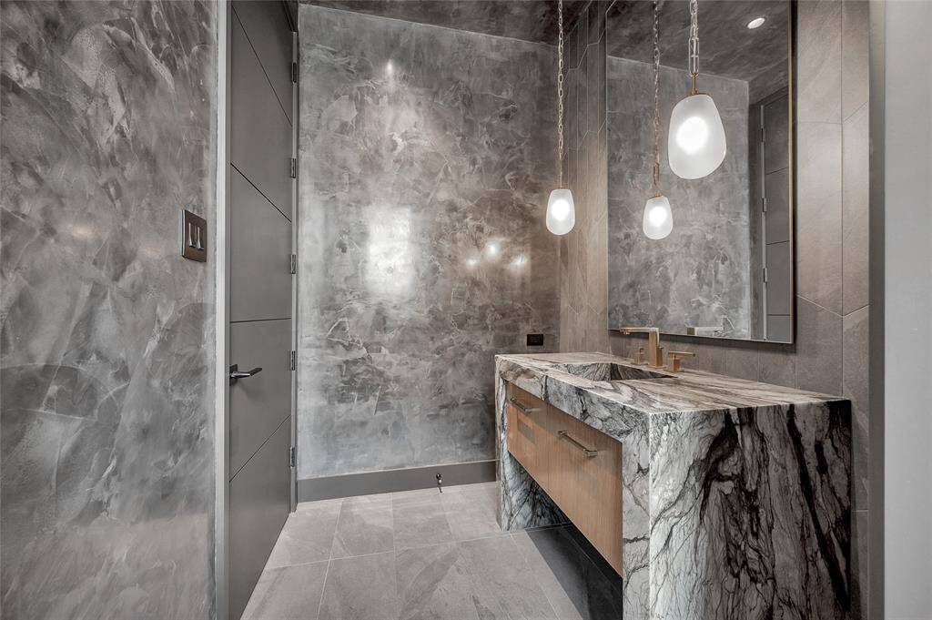 [Formal Powder Room]Sophisticated amenities include a waterfall sink cabinet, a custom-designed stone accent wall, Venetian plaster walls, and Circa lighting.