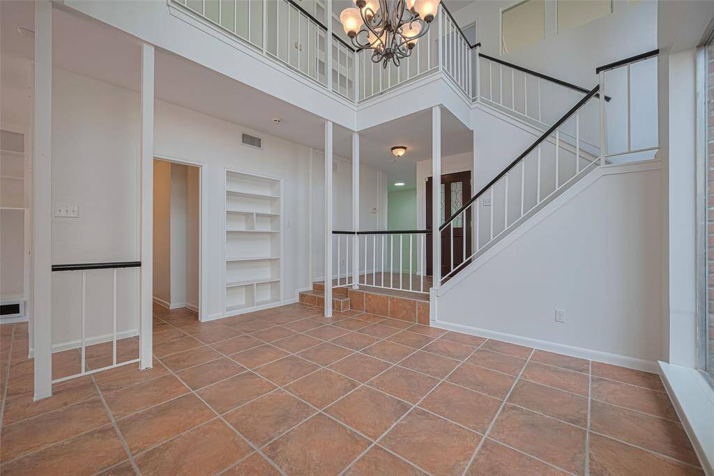 The dining room features a two-story ceiling with chandelier and a wall of windows looking out onto foliage.