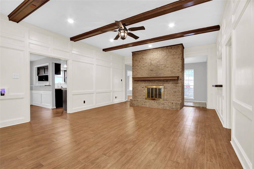Experience the charm of this inviting den, boasting a classic brick fireplace and rich wooden beams, all complemented by elegant white paneling.